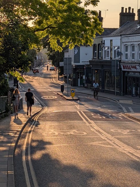 A pedestrian green light is illuminated at a traffic intersection on Cambridge Heath Road, with traffic signals and a black metal traffic pole visible in the foreground. To the left, part of a black v